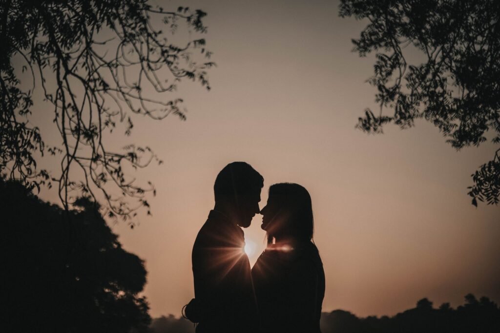 Silhouette of a couple embracing at sunset, creating a romantic scene with sunbeam highlights.