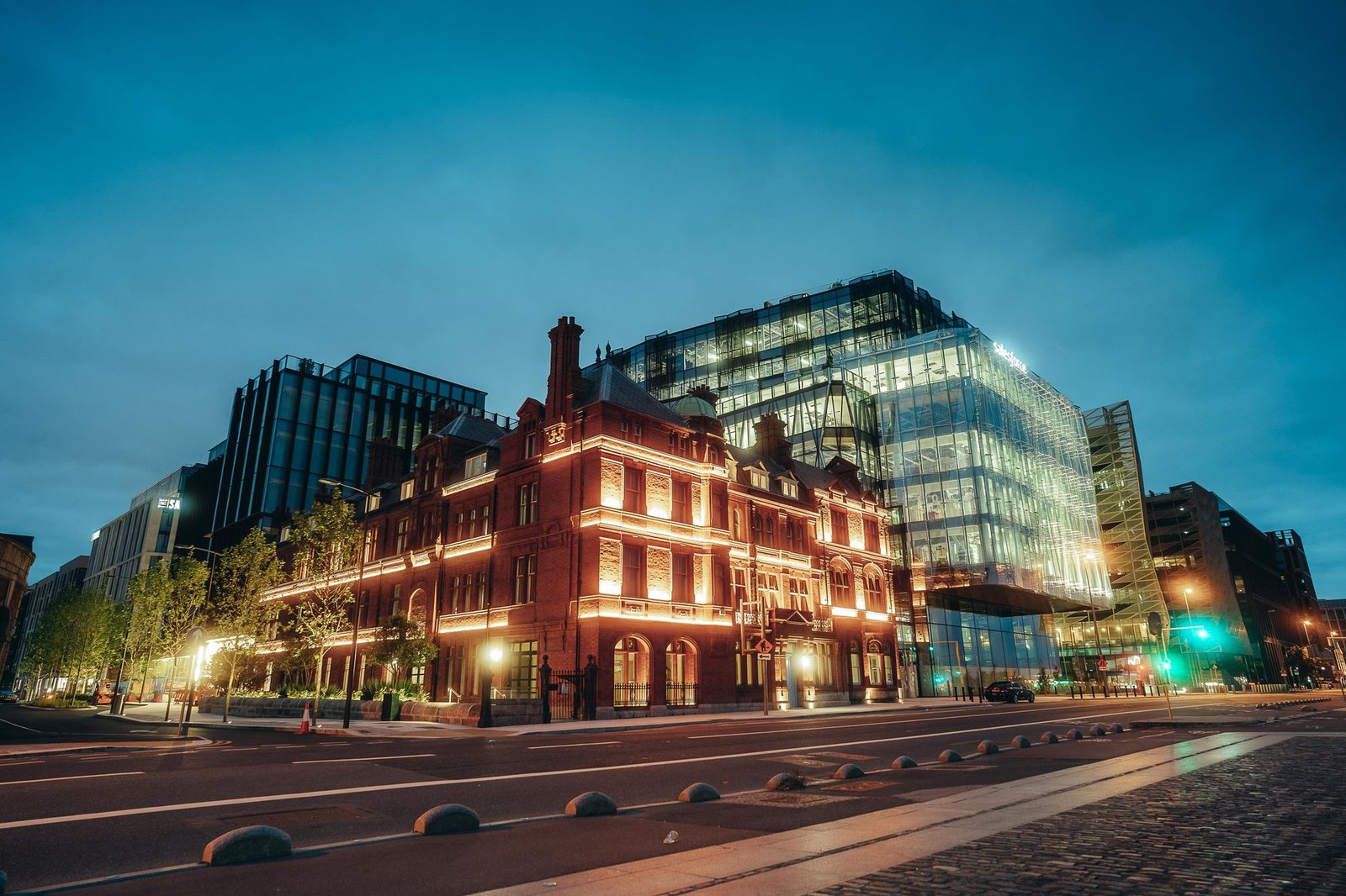 A vibrant cityscape at night showcasing historic and modern architecture under a deep blue sky.
