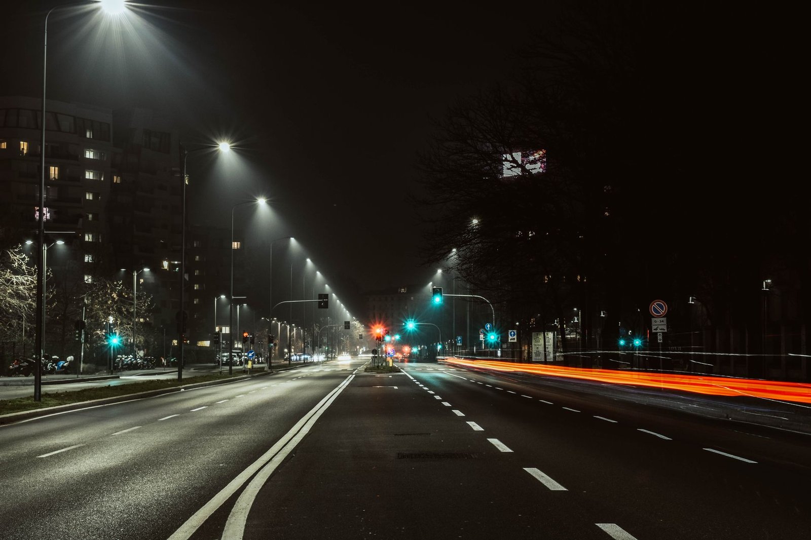 A vibrant city street at night, illuminated by streetlights and streaks of light from passing traffic.