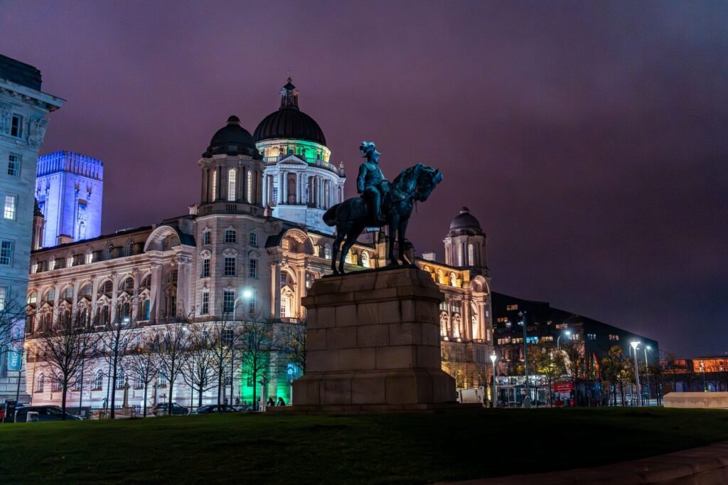 Night view of Liverpool cityscape featuring an iconic statue and illuminated historic building.