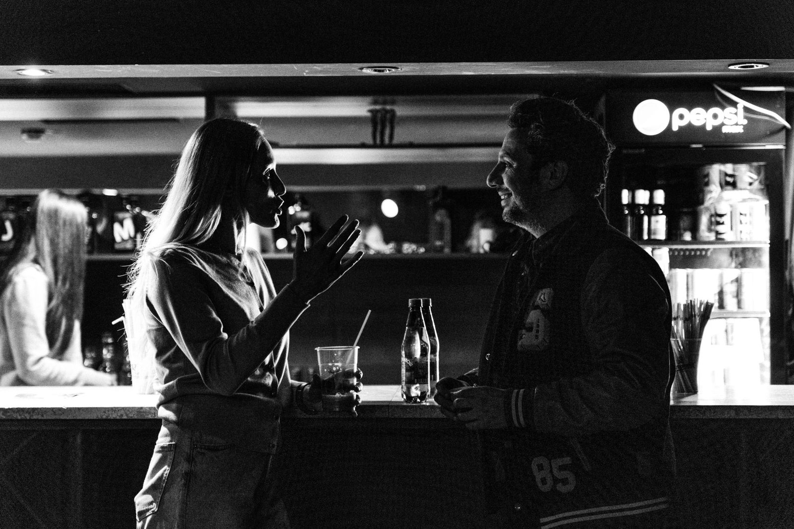 Monochrome photo of a man and woman talking at a bar, capturing an intimate social moment.