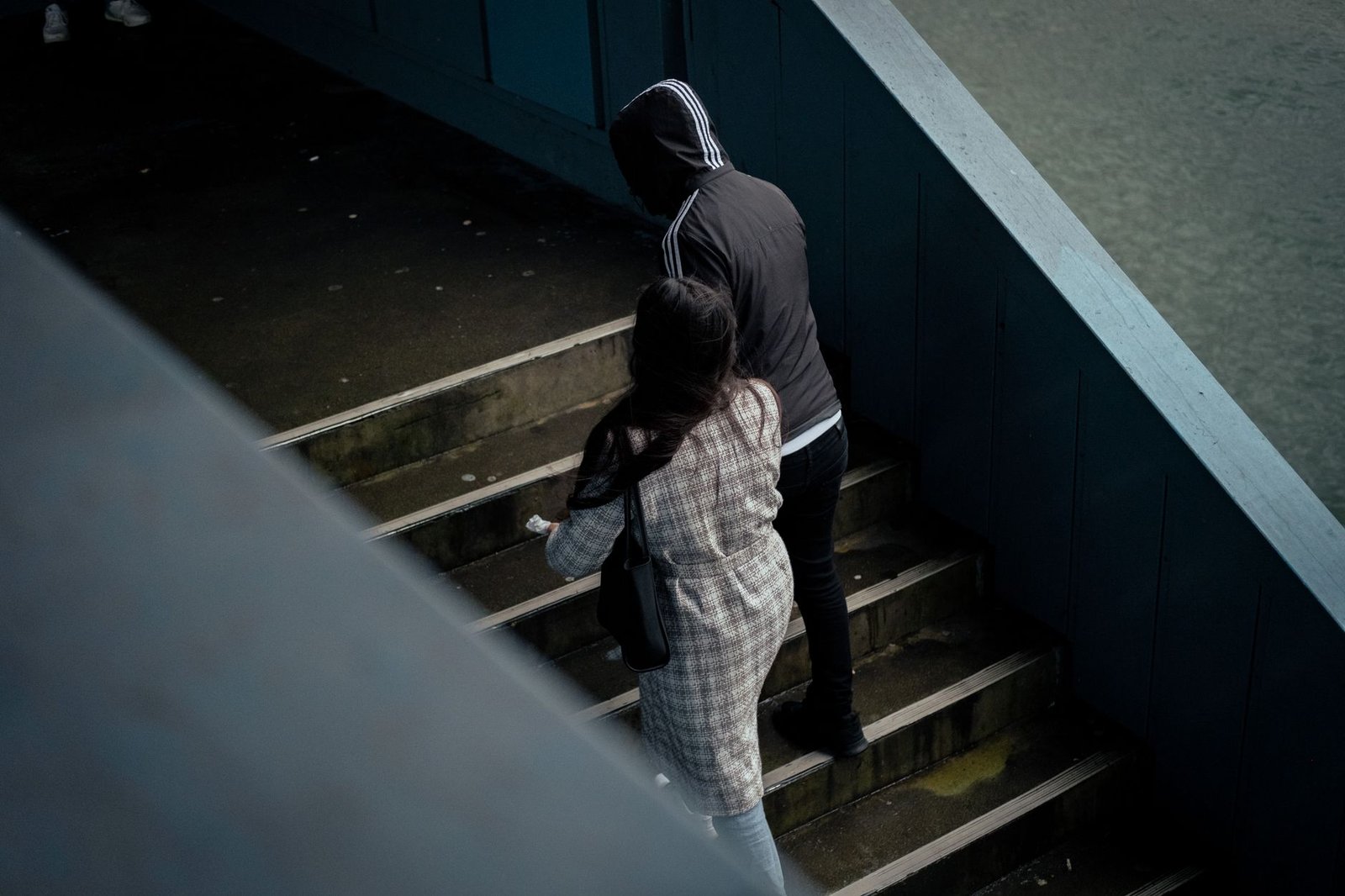 Two people ascend an outdoor staircase on a cloudy day. Urban setting, moody vibe.