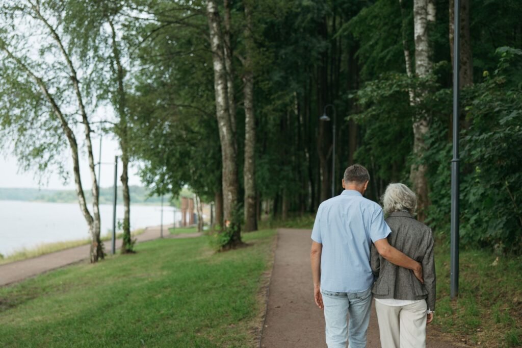 Senior couple strolls arm-in-arm on a tranquil forest pathway, embodying love and togetherness.