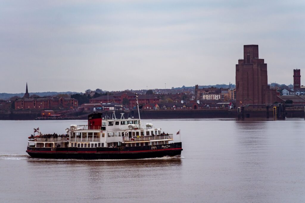 A ferry sails on the Mersey River in Liverpool with landmarks in the background.