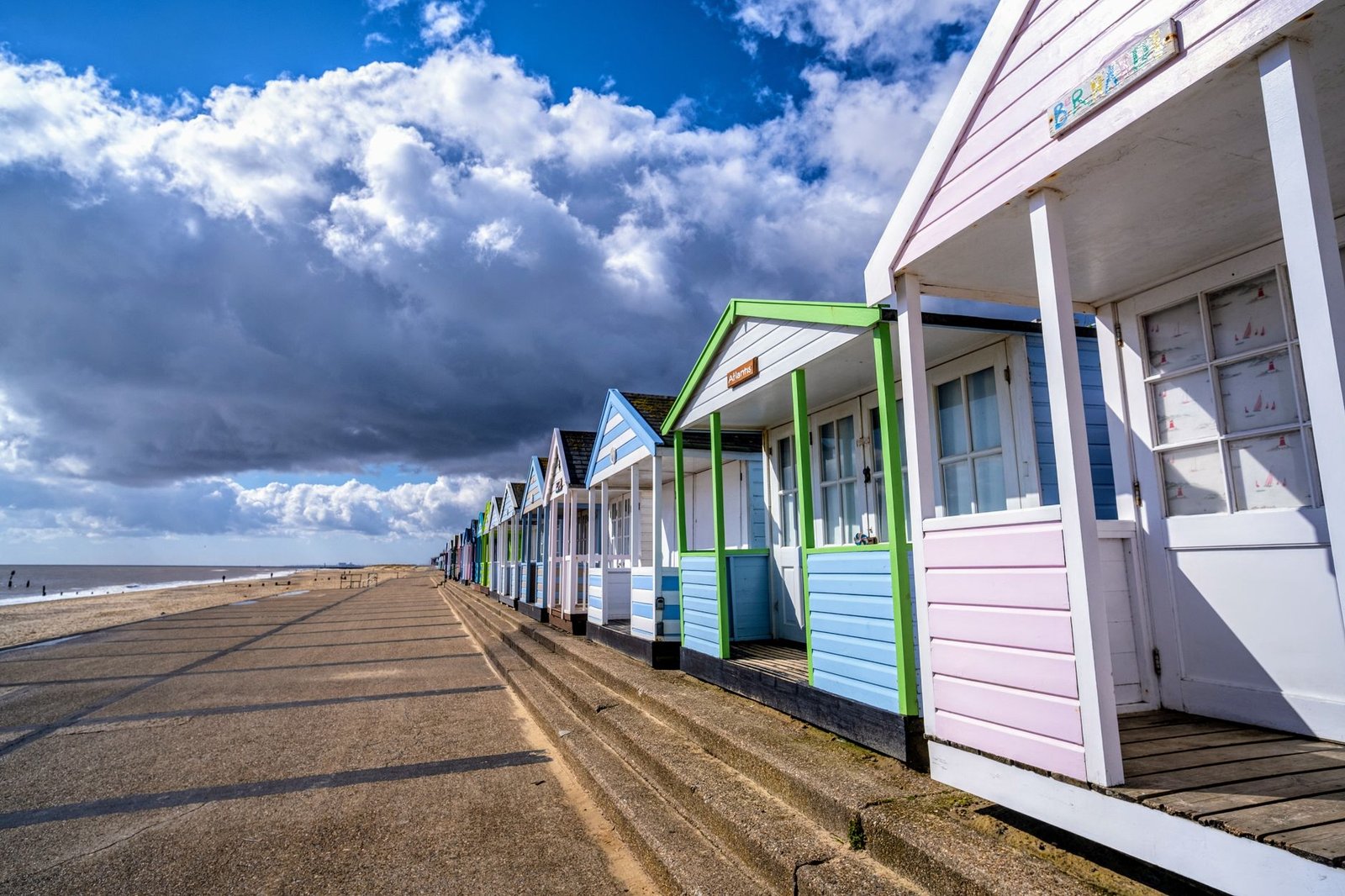 Charming pastel beach huts lined up on the Southwold promenade, under a dramatic sky.