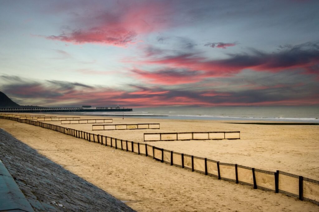 Serene beach with dramatic pink clouds and calm sea waters during sunset.