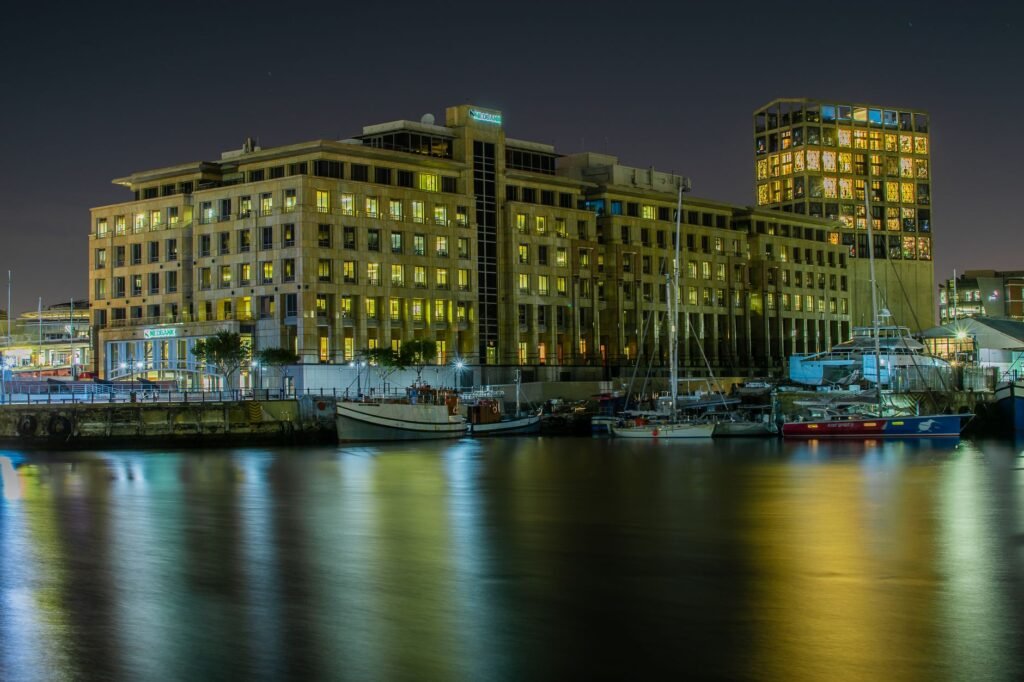Illuminated buildings reflecting on calm waters at night in Cape Town, South Africa.