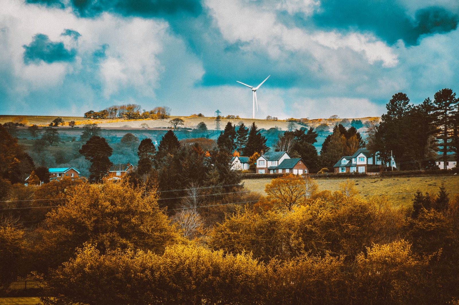 Picturesque village with autumn foliage and a wind turbine under a dramatic sky.