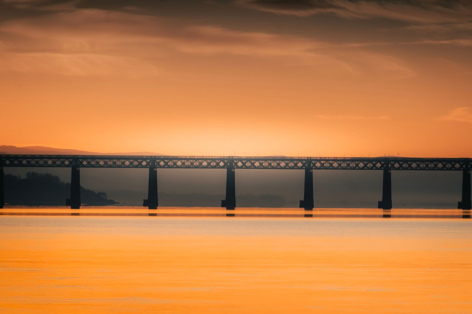 Breathtaking sunset over a scenic rail bridge in Scotland, featuring vibrant orange hues.
