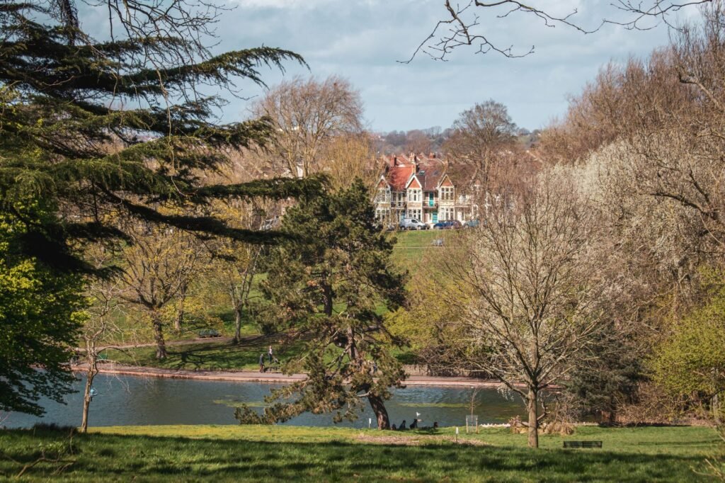 Scenic view of a lush park with a historic building in the background, surrounded by trees and a tranquil lake.