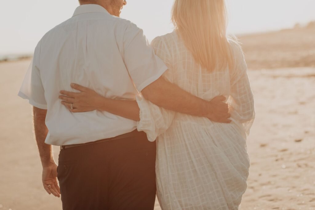 A loving couple walking arm-in-arm on a sunny beach during sunset.