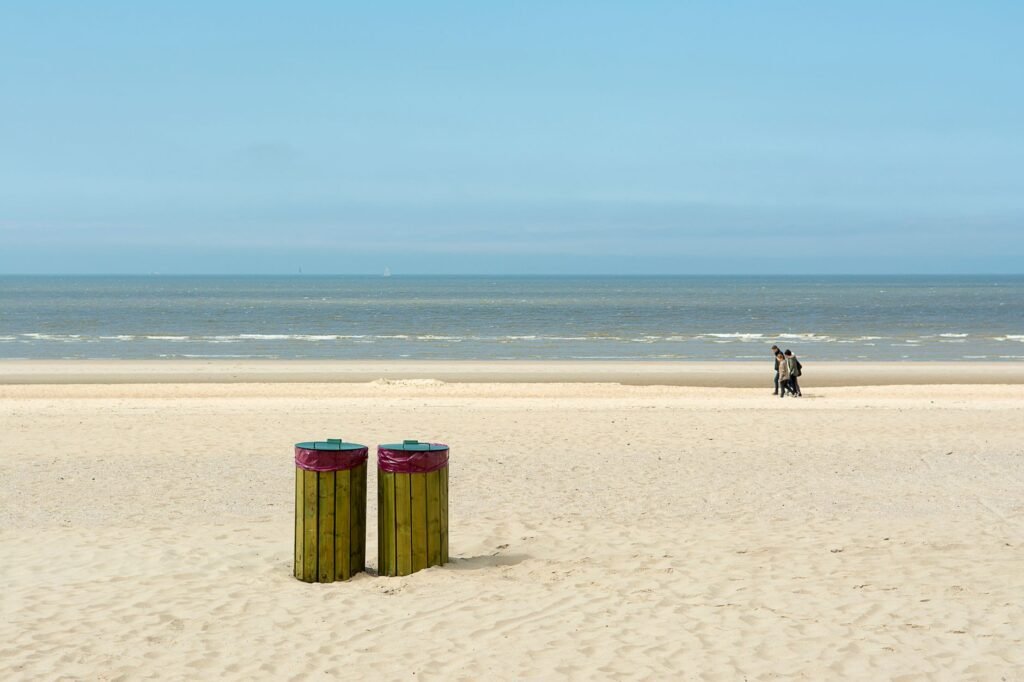 Serene beach landscape featuring two trash bins and a couple walking by the shore.