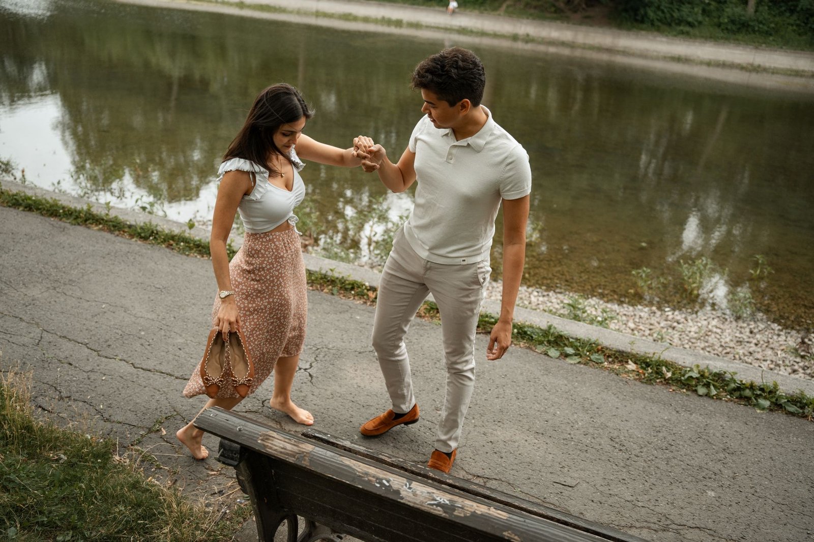 A couple walking hand in hand by a riverside park, enjoying a peaceful day outdoors.