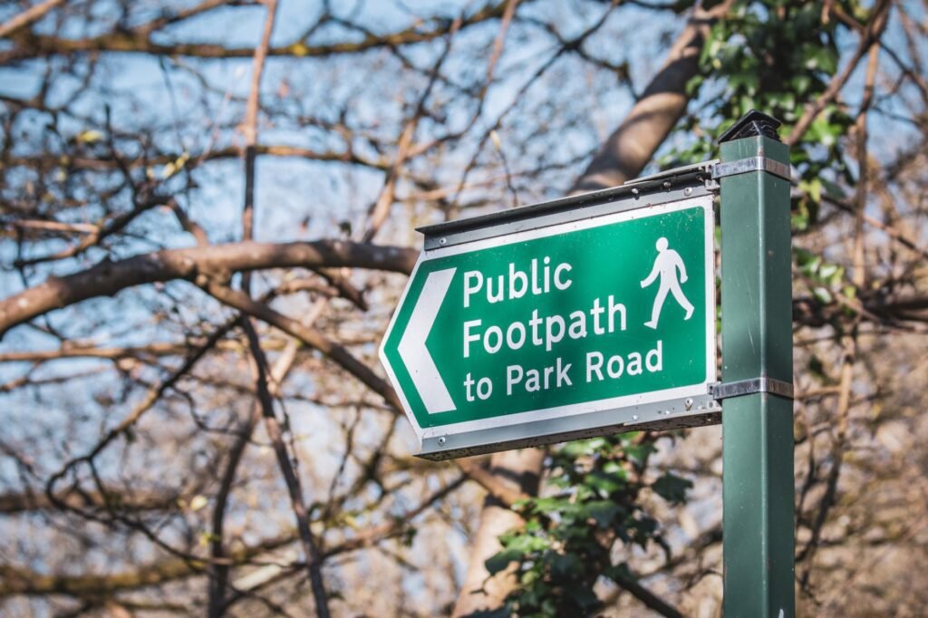 Green public footpath sign in a Bristol park, guiding pedestrians with trees in the background.