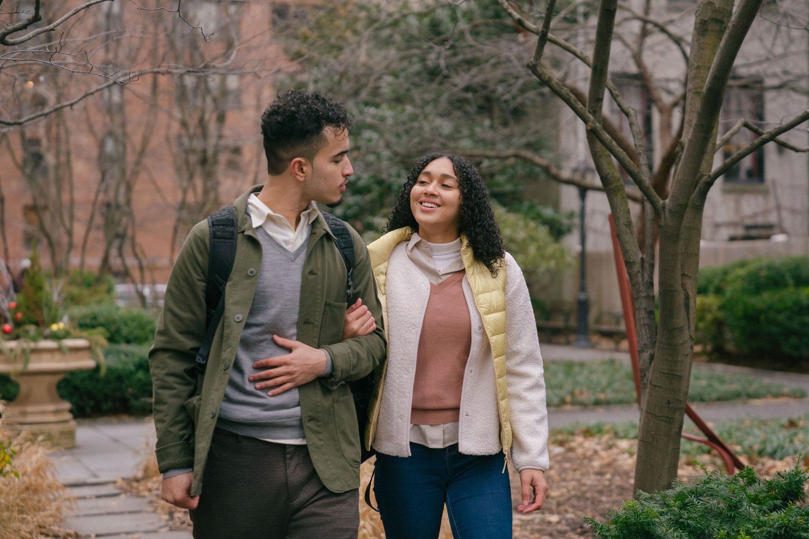 Young Hispanic couple in casual outfit walking in park on walkway while having date and holding hands and looking at each oth