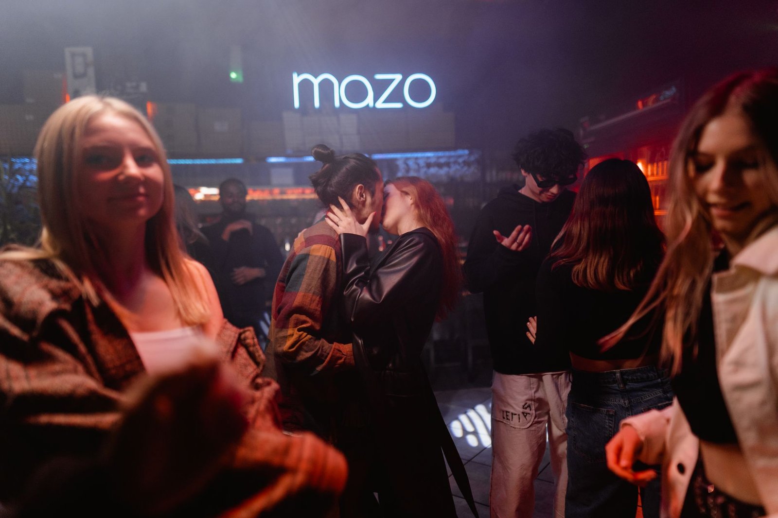 Group of young adults enjoying a night out at a lively club, with a couple kissing and friends mingling.