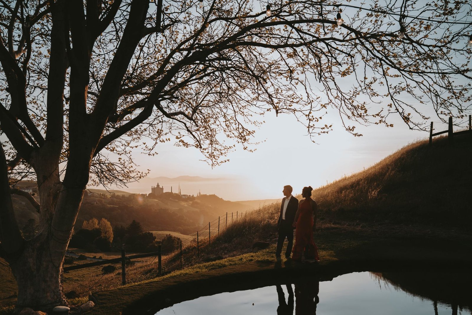 A couple elegantly walking near a pond against a sunset backdrop in Fremont, California.
