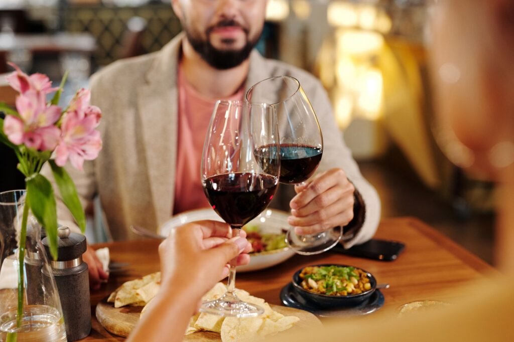 A couple toasts with red wine at a cozy restaurant table, surrounded by flowers and appetizers.