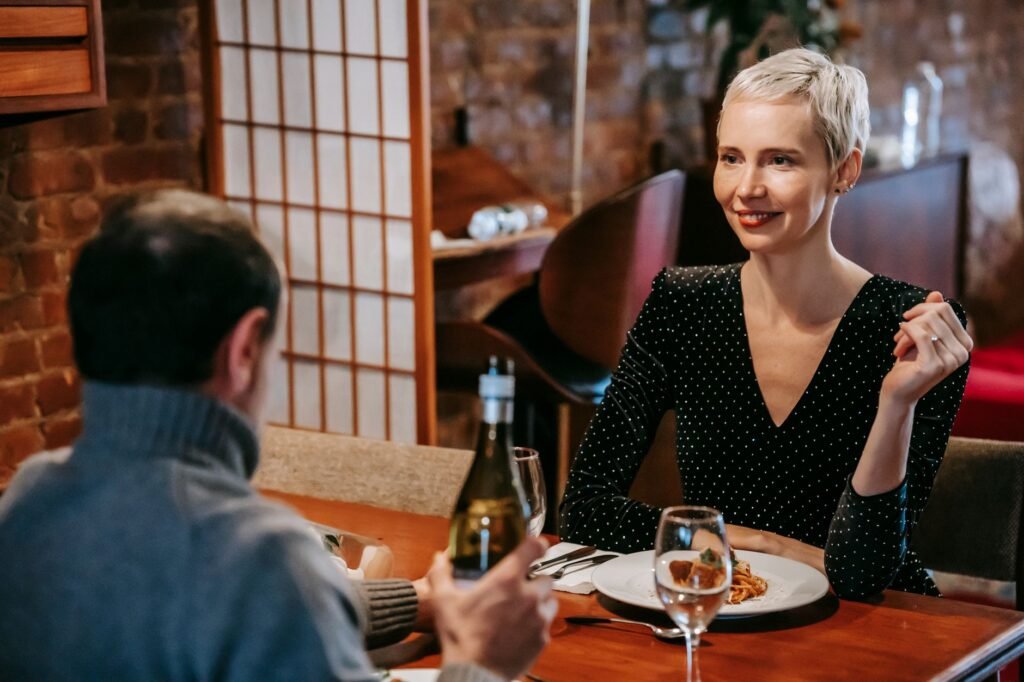 Positive couple sitting at table while having date in bright restaurant with pasta with meatballs on plate with glasses and w