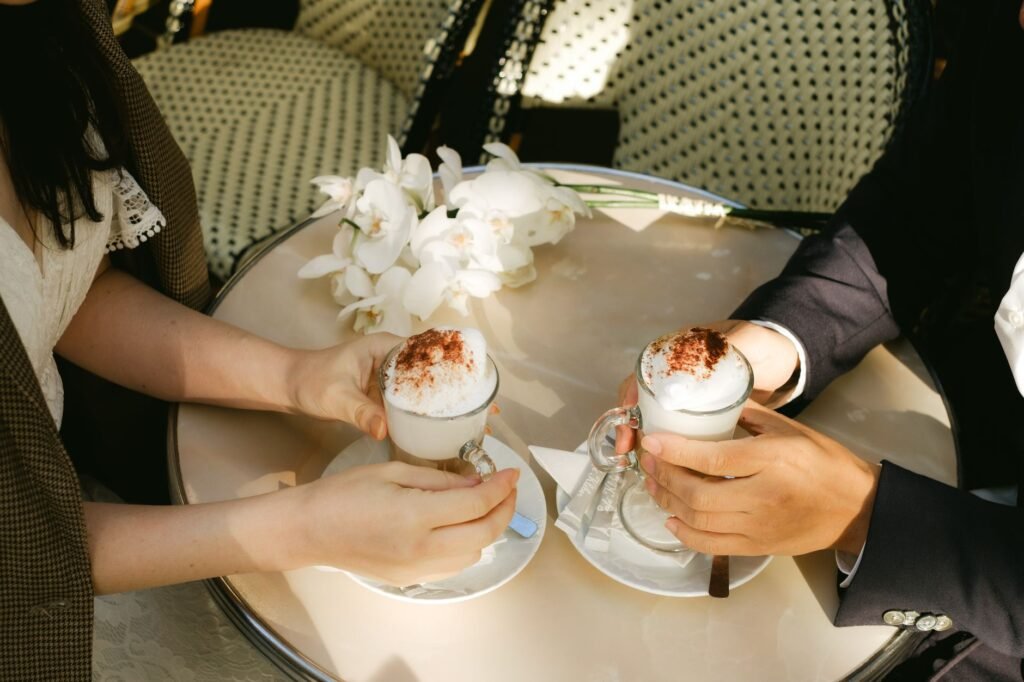 Two people enjoying cappuccinos at an outdoor café table adorned with white flowers.