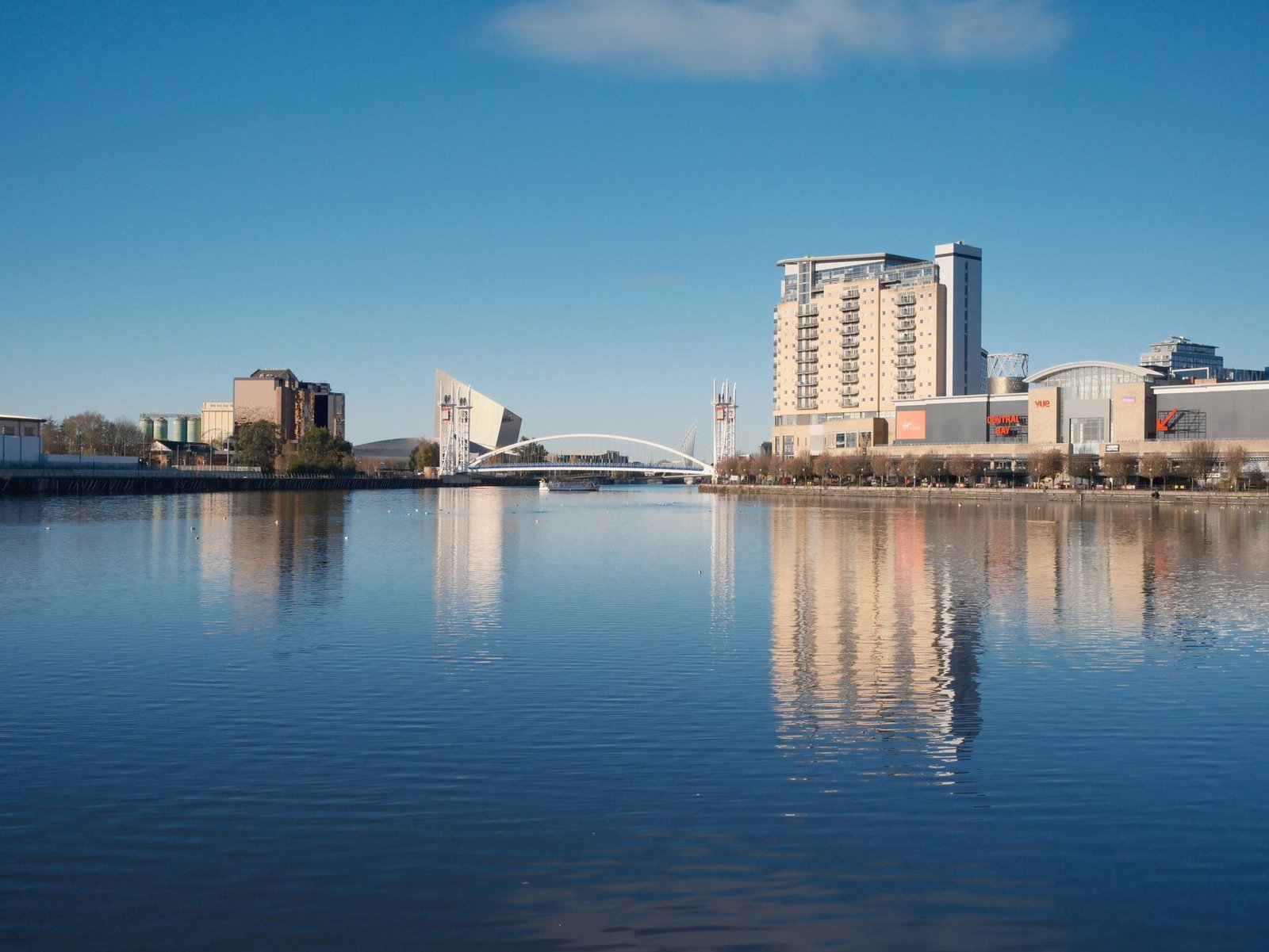 A scenic view of Dublin's waterfront with modern architecture and calm river reflections under a clear blue sky.