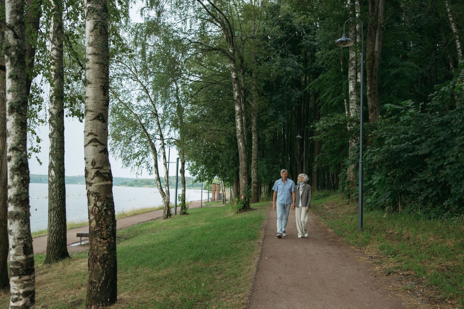 A senior couple enjoys a peaceful walk along a tree-lined path in a serene park setting.