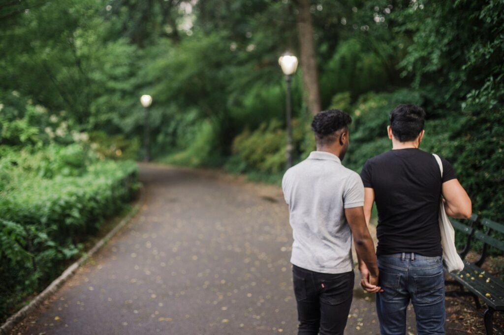 A couple holding hands walking on a serene forest pathway during the day.