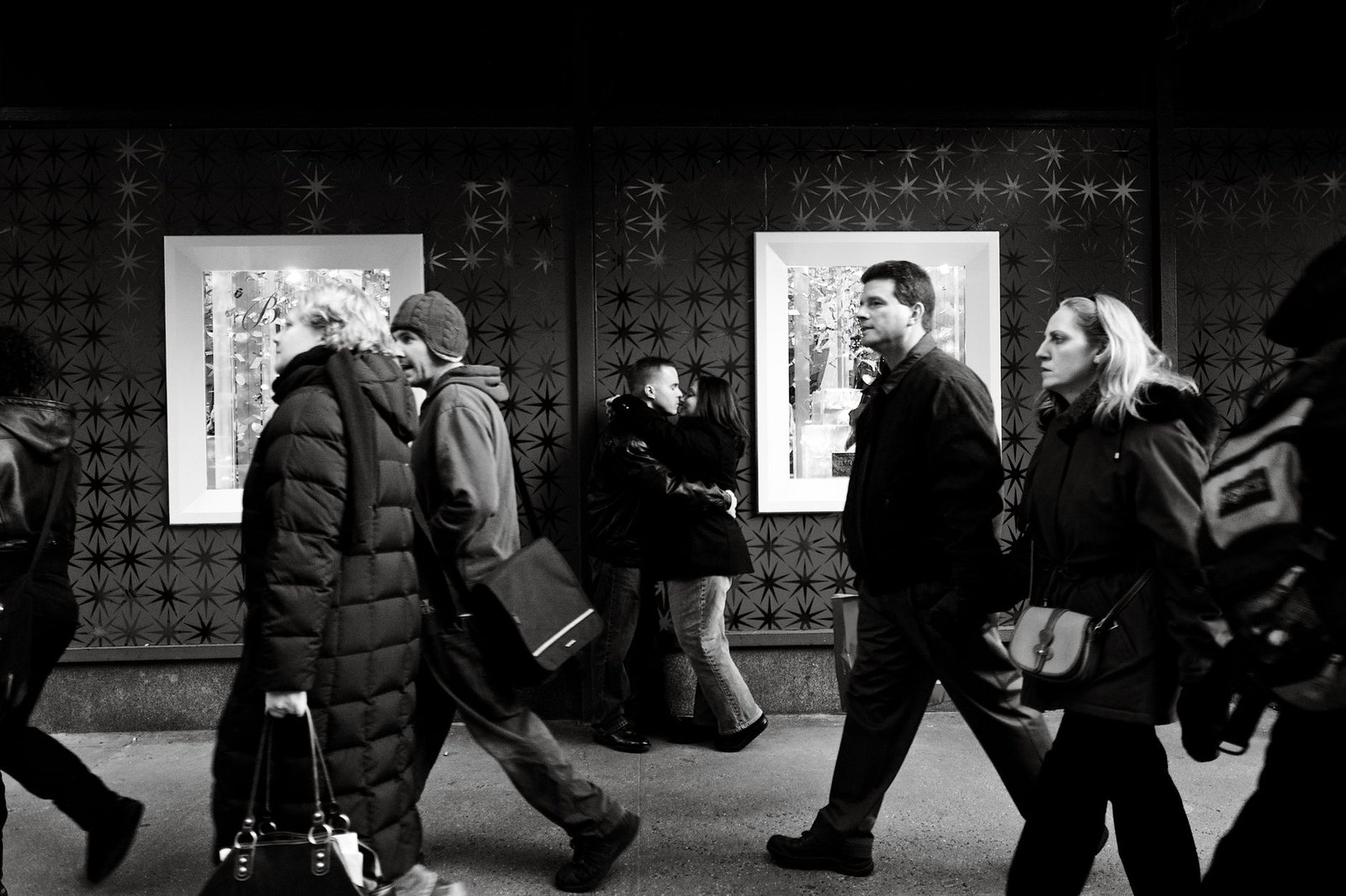 Black and white street scene in New York City featuring diverse pedestrians walking past art displays.
