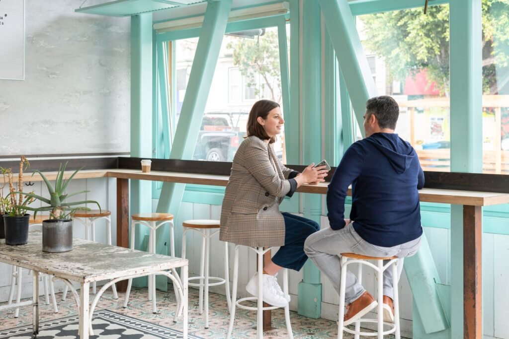 A man and woman have a casual conversation in a bright, modern cafe.