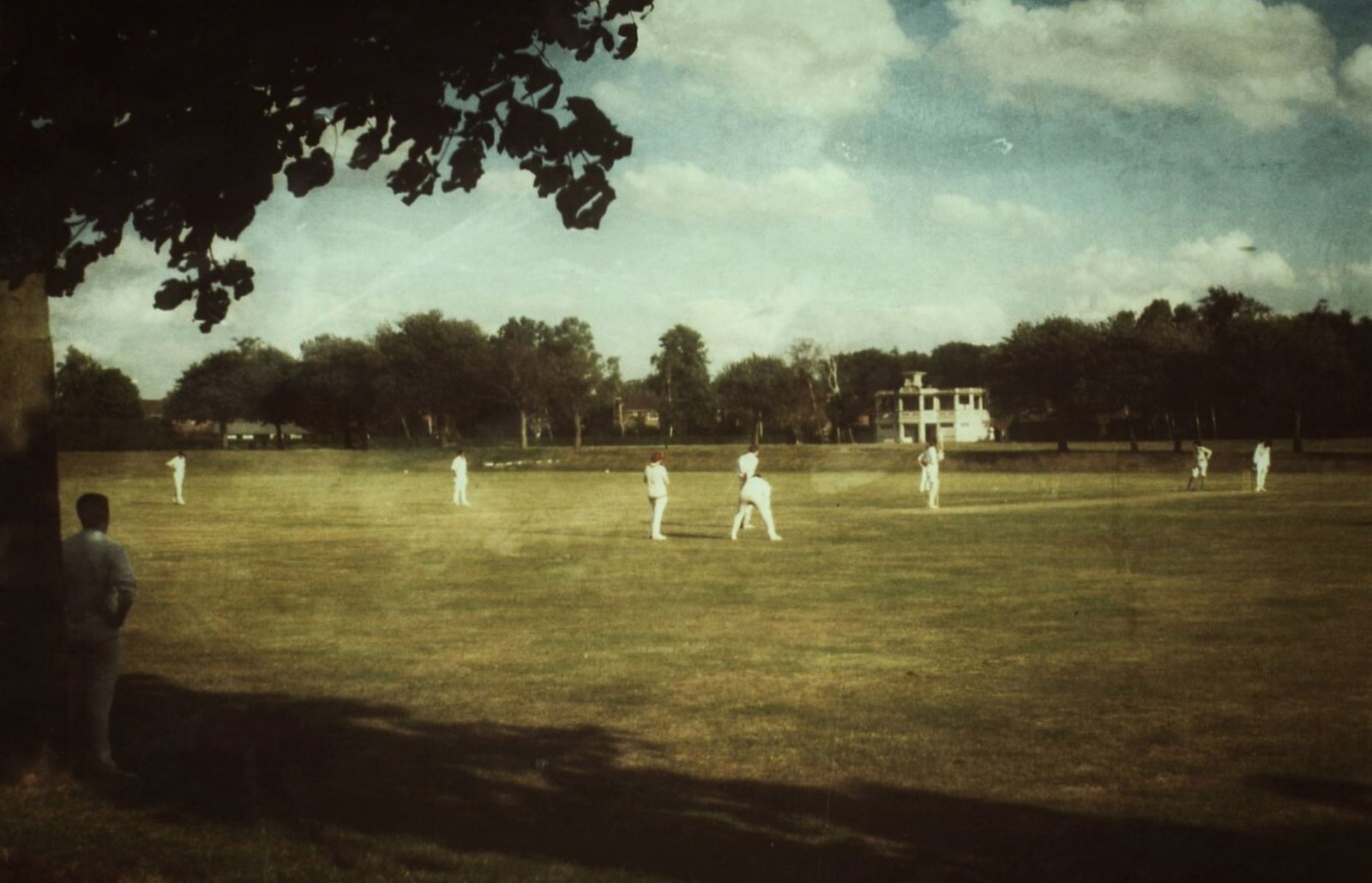 A vintage-style photo capturing a cricket match in a park in Norwich, England.