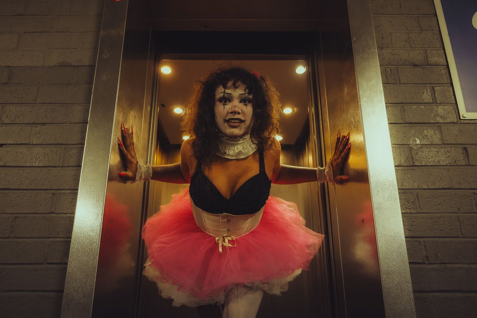 A person in clown makeup and tutu costume emerging from an elevator, showcasing gothic and horror aesthetics.