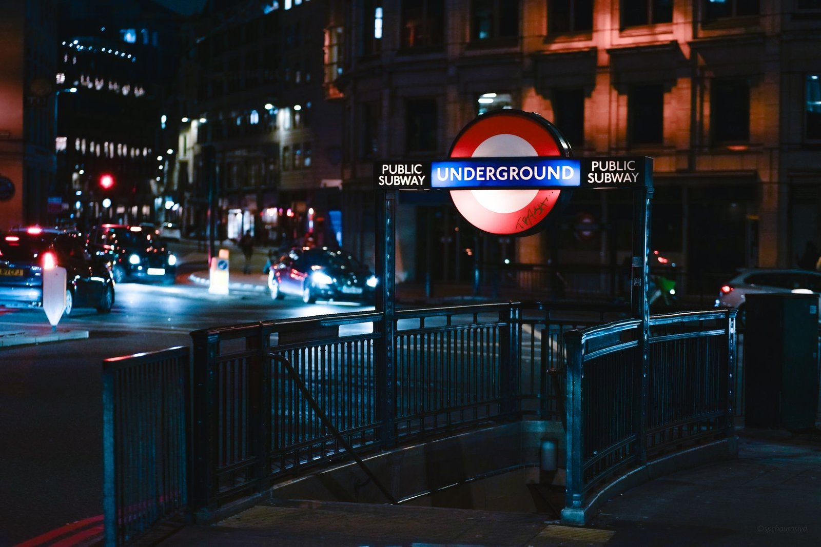 Moody night shot capturing an illuminated London Underground entrance with city lights.