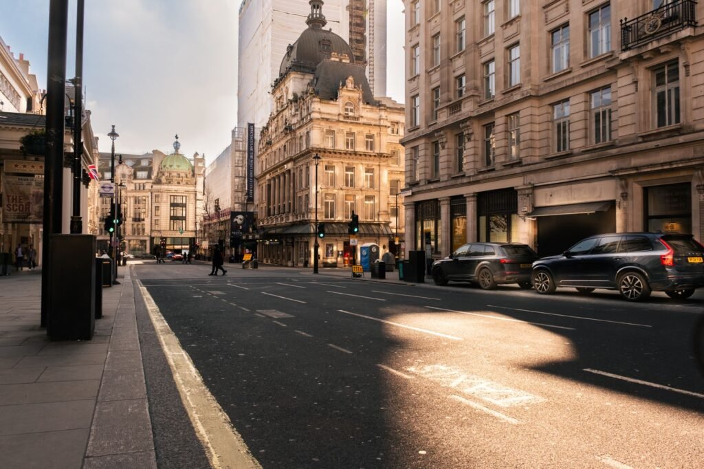 A sunlit street in London's historic district, showcasing Victorian architecture and modern vehicles.