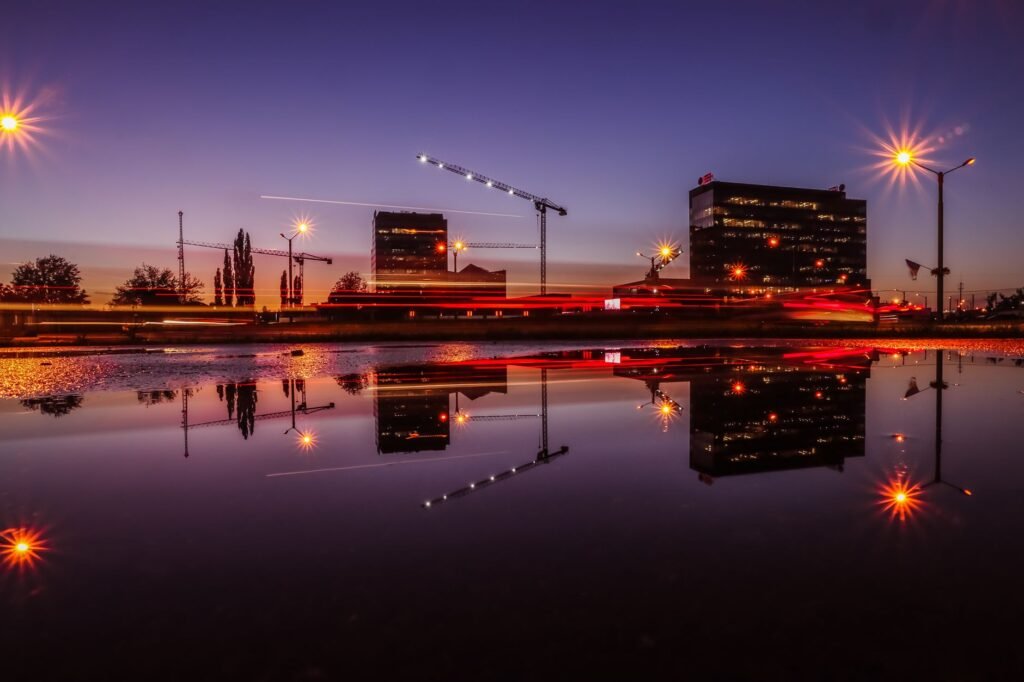 City skyline at dusk with colorful reflections in water, capturing urban lights and architecture.