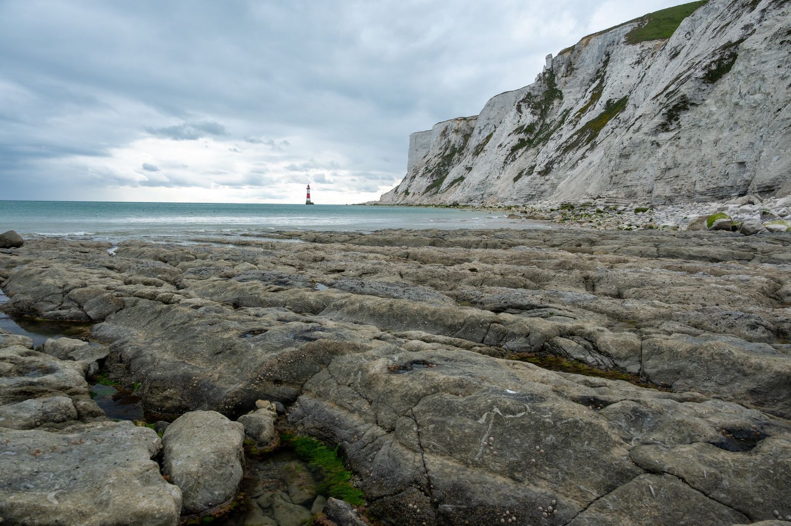Stunning view of Beachy Head cliffs and lighthouse under a cloudy sky on the English coast.