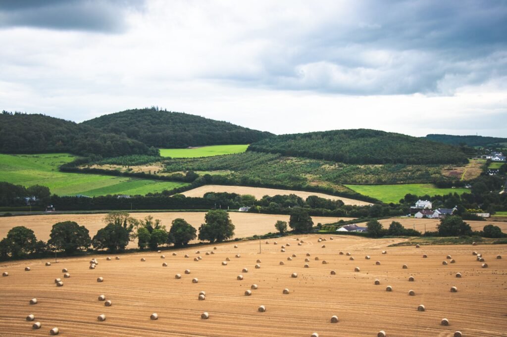 Wide view of a lush Irish landscape featuring hay bales and green rolling hills under a cloudy sky.