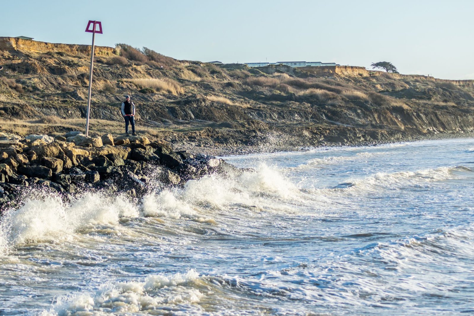 Man standing on rocky coastline with waves crashing at seaside cliffs in England.
