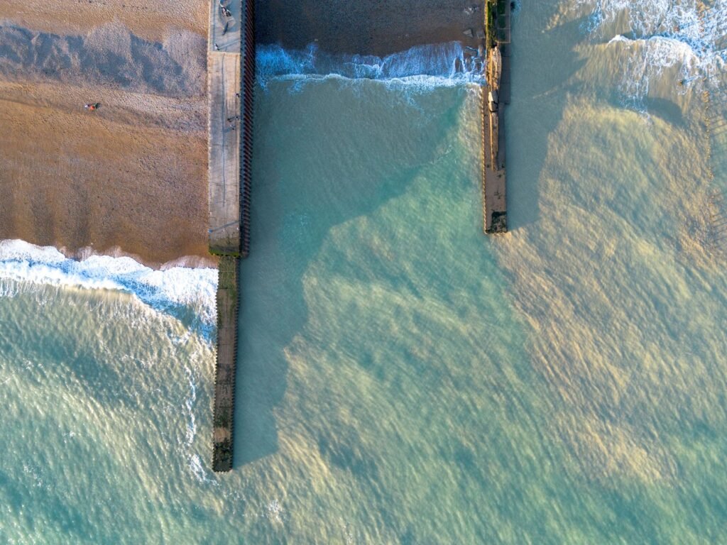 Aerial snapshot of East Sussex coastline featuring piers and sandy beach in England.