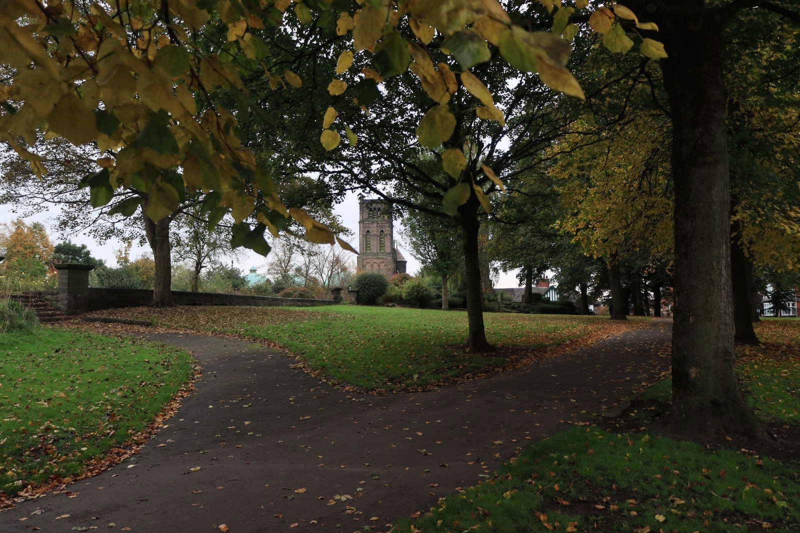Charming autumn scene with pathways and historic church tower in an English park.