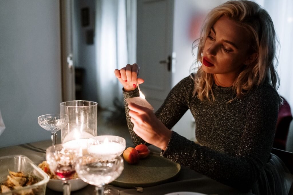 A woman prepares a cozy candlelit dinner table for a special evening indoors.