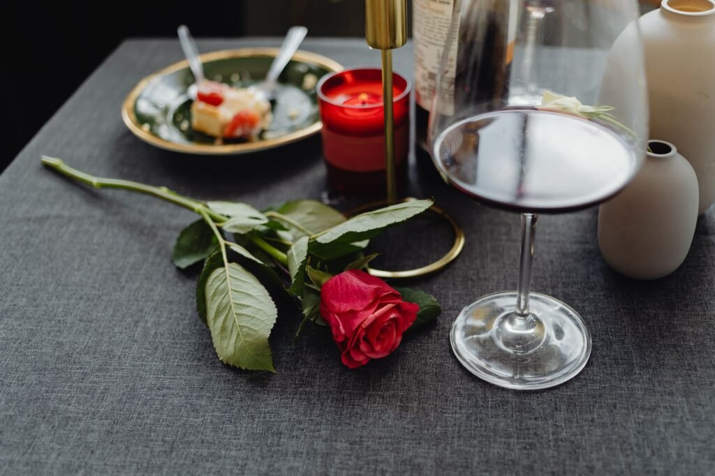 Elegant table setup with wine, candle, and red rose for a romantic evening.