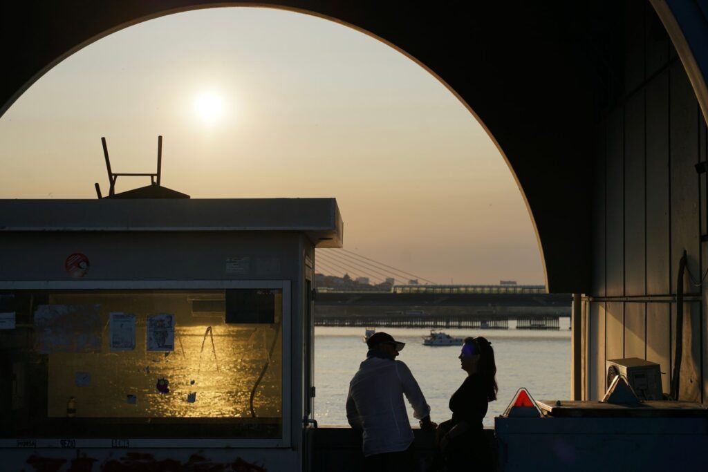 Silhouetted couple enjoying sunset by the waterfront with urban skyline.