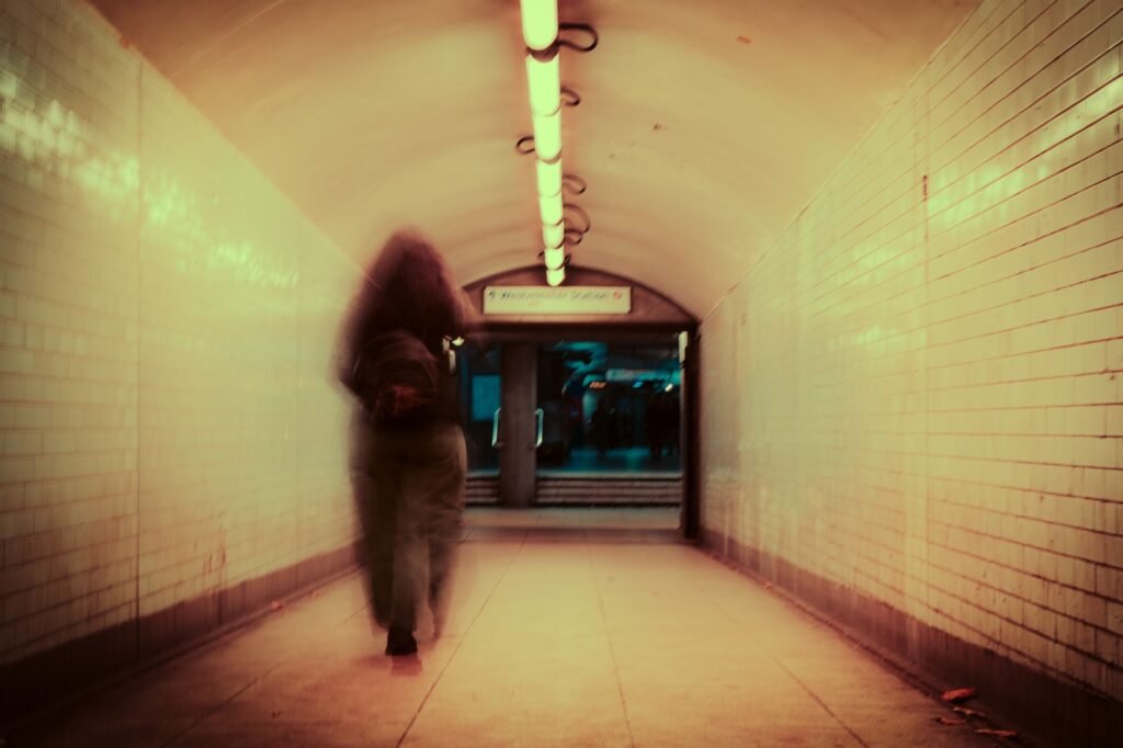 Blurred figure walking in a dimly lit London underground tunnel, creating a moody and mysterious atmosphere.