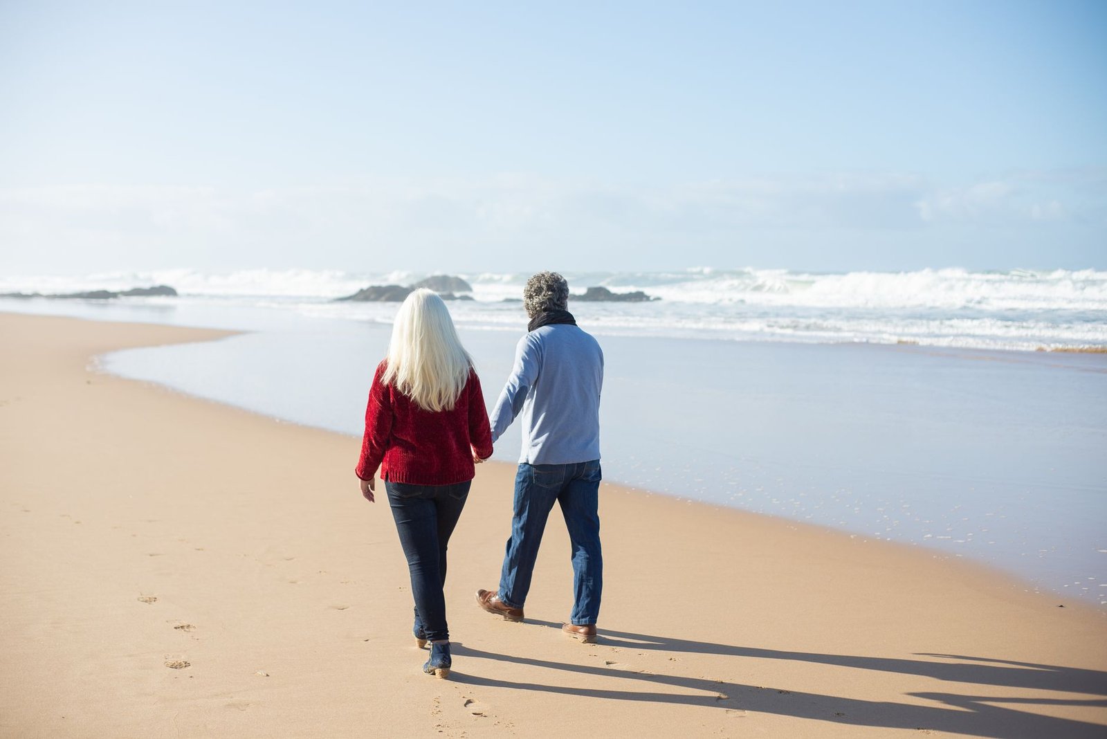 A couple walks hand in hand on a sandy beach with the ocean waves gently crashing nearby in Portugal.