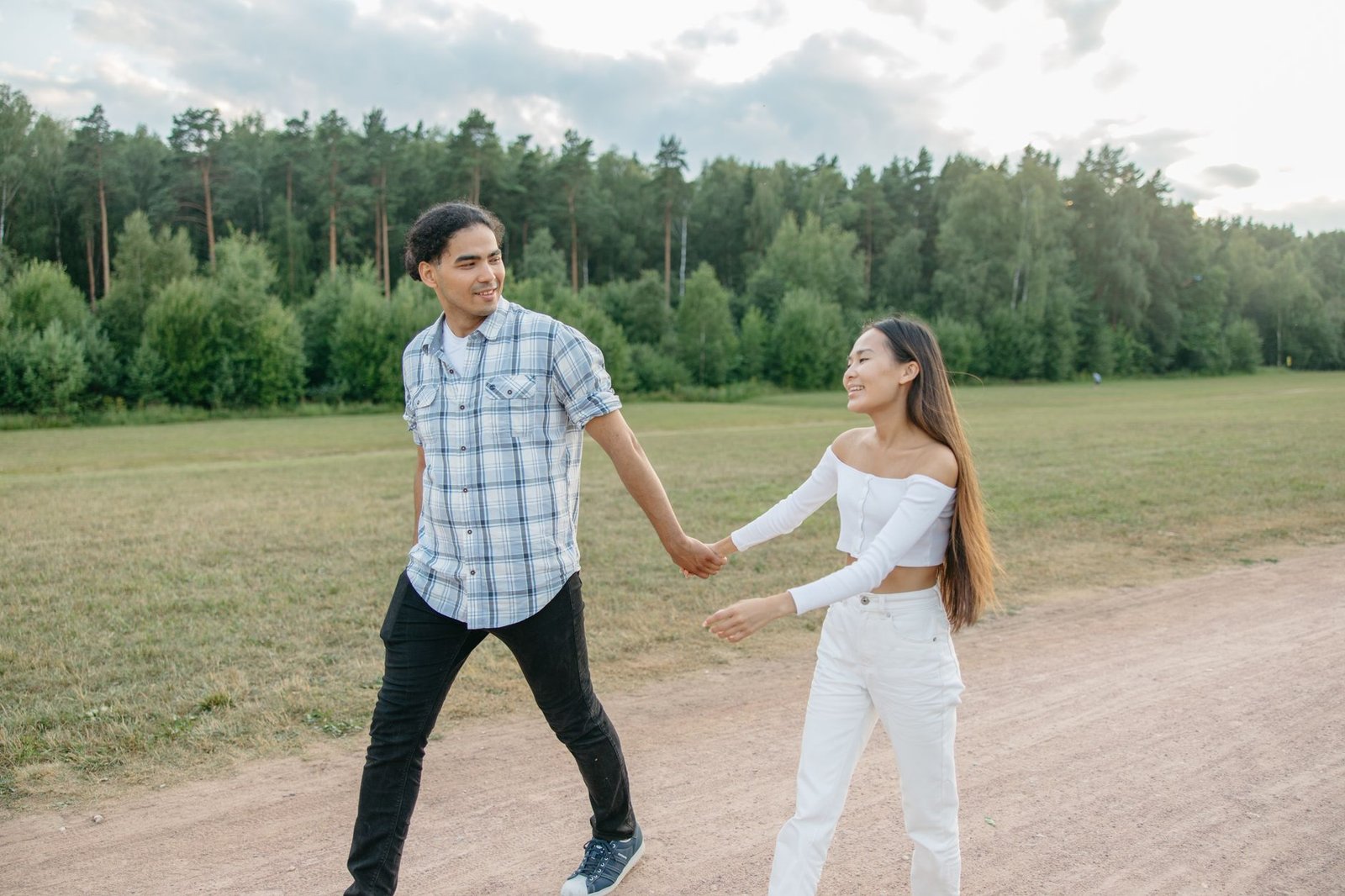 Joyful couple walking hand in hand through a lush park setting, under a bright sky.