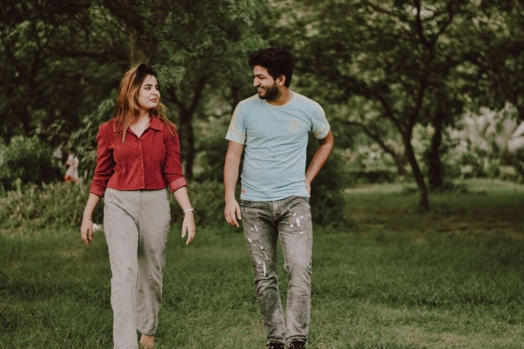 Cheerful young ethnic man and woman in casual clothes walking on grassy lawn while spending time together in green park