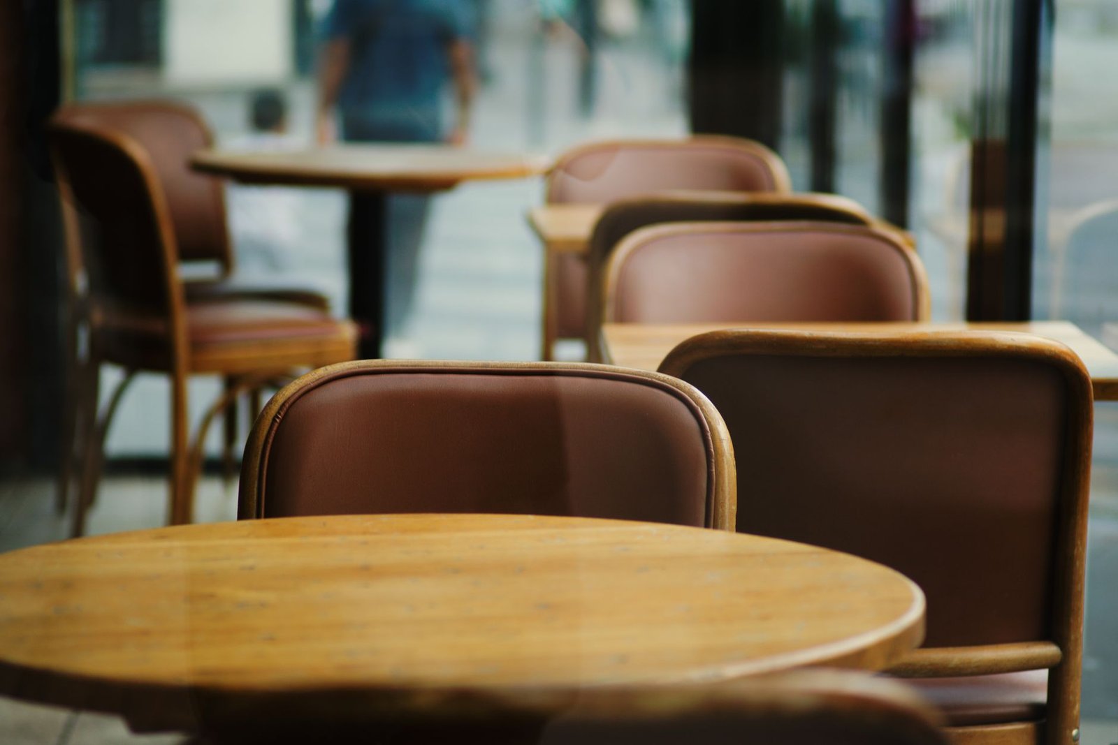 A serene cafe interior featuring empty wooden tables and leather chairs, ideal for dining settings.