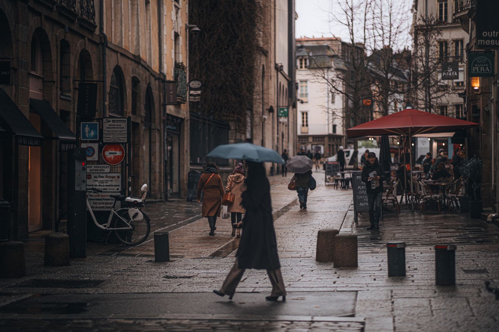 People walking with umbrellas on a rainy street in Europe, capturing a cozy urban vibe.