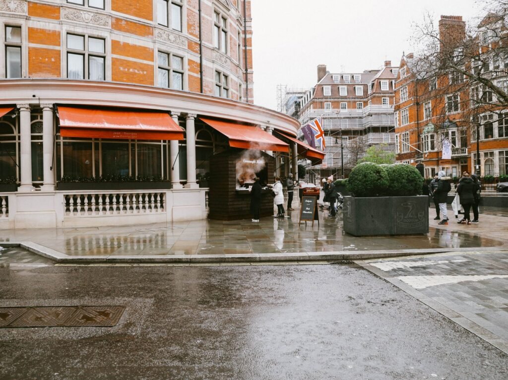A street scene in London with people, wet pavement, and iconic architecture on a rainy day.