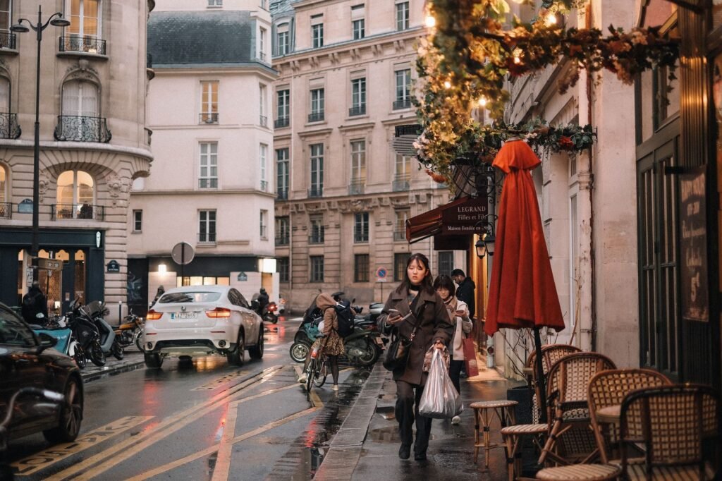 Cozy Paris city street with people, cars, and festive lights on a rainy day.